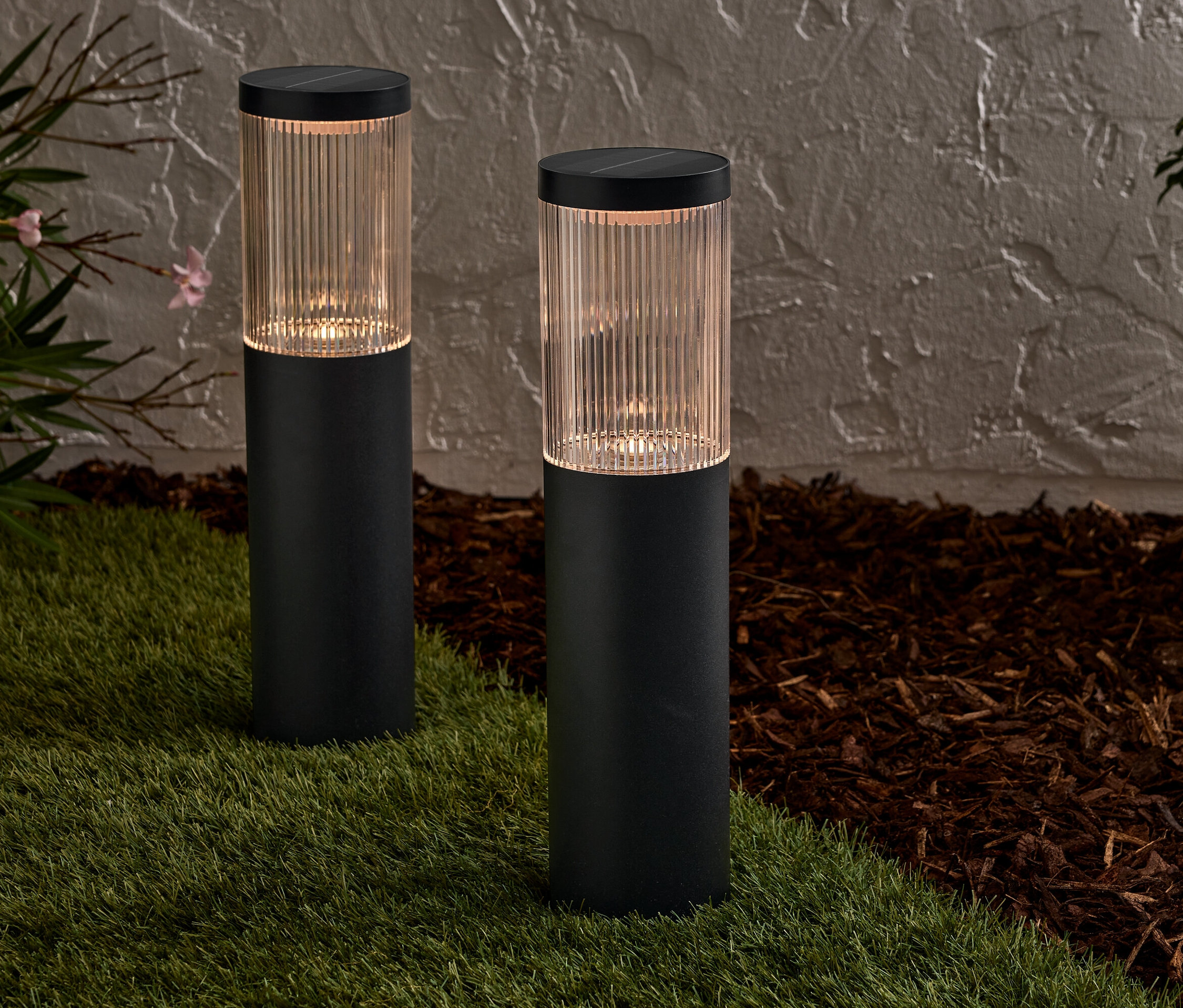 Dwie czarne lampy solarne stoją na trawniku przed ścianą.