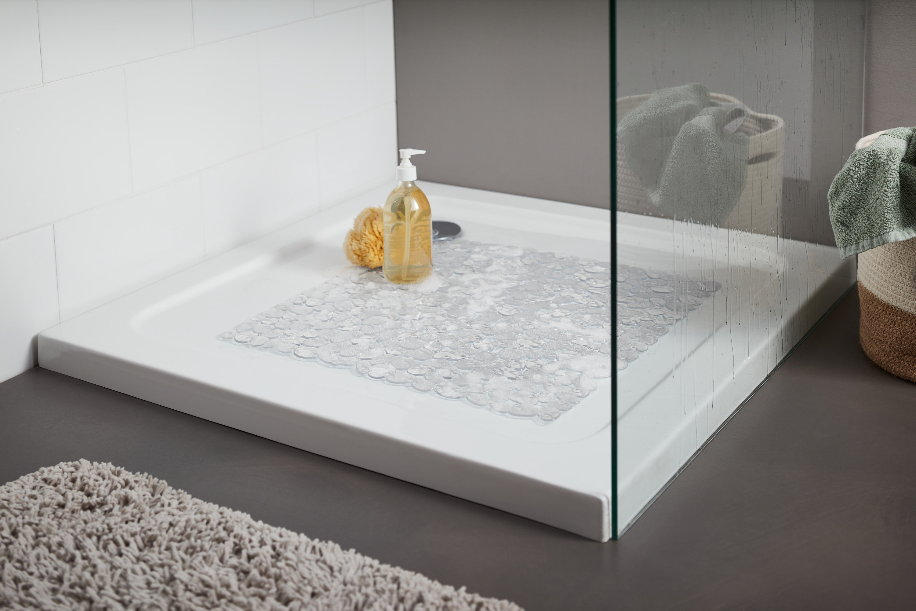 Brodzik z przezroczystą matą do brodzika. Na brodziku leży żółta gąbka do kąpieli i butelka z pompką.