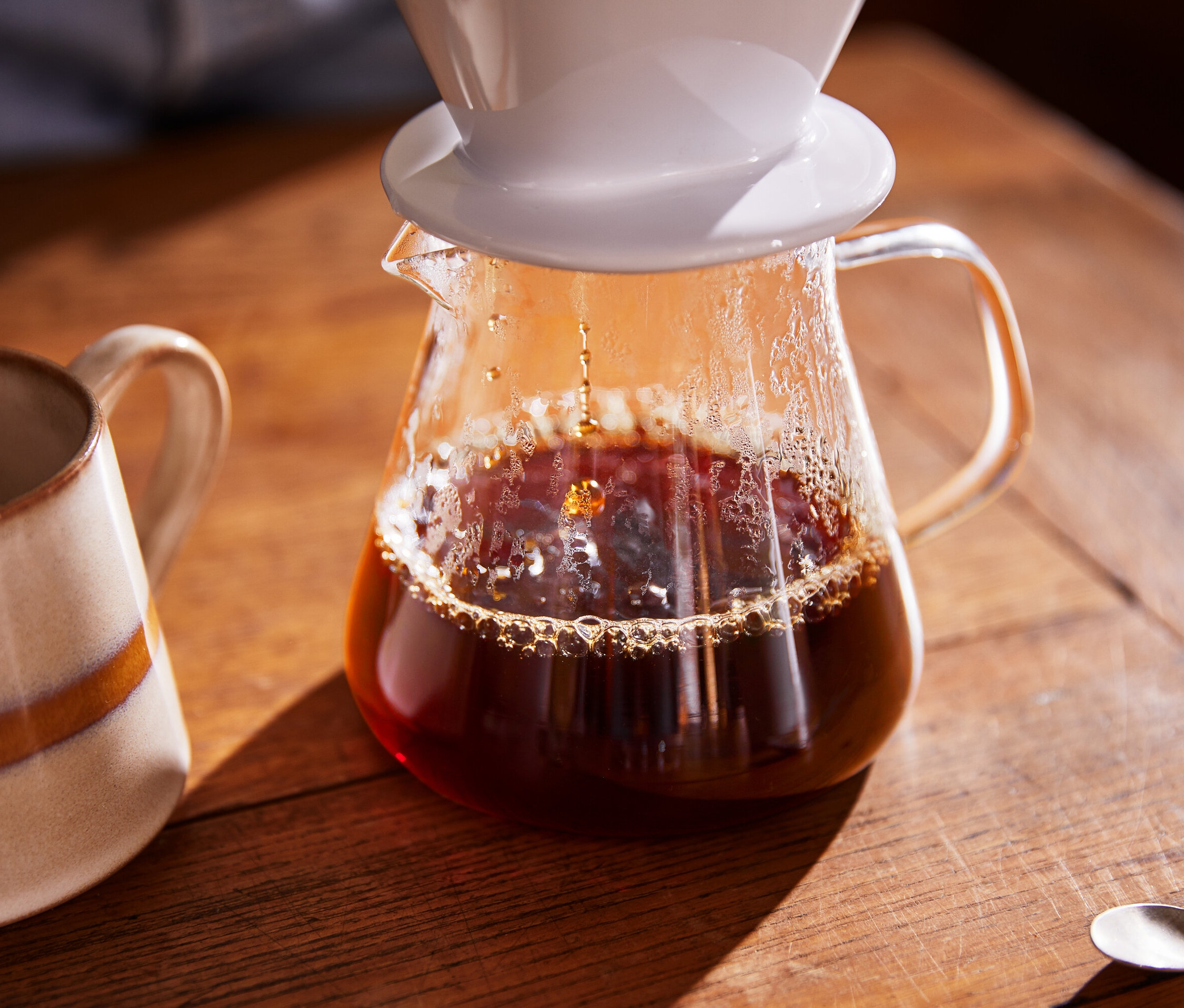 Kawa wlewa się do szklanego dzbanka do kawy, obok stoi kubek.