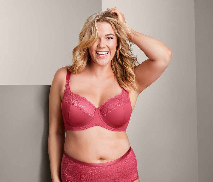 Uśmiechnięta kobieta pozuje w malinowym biustonoszu z fiszbinami i majtkach.