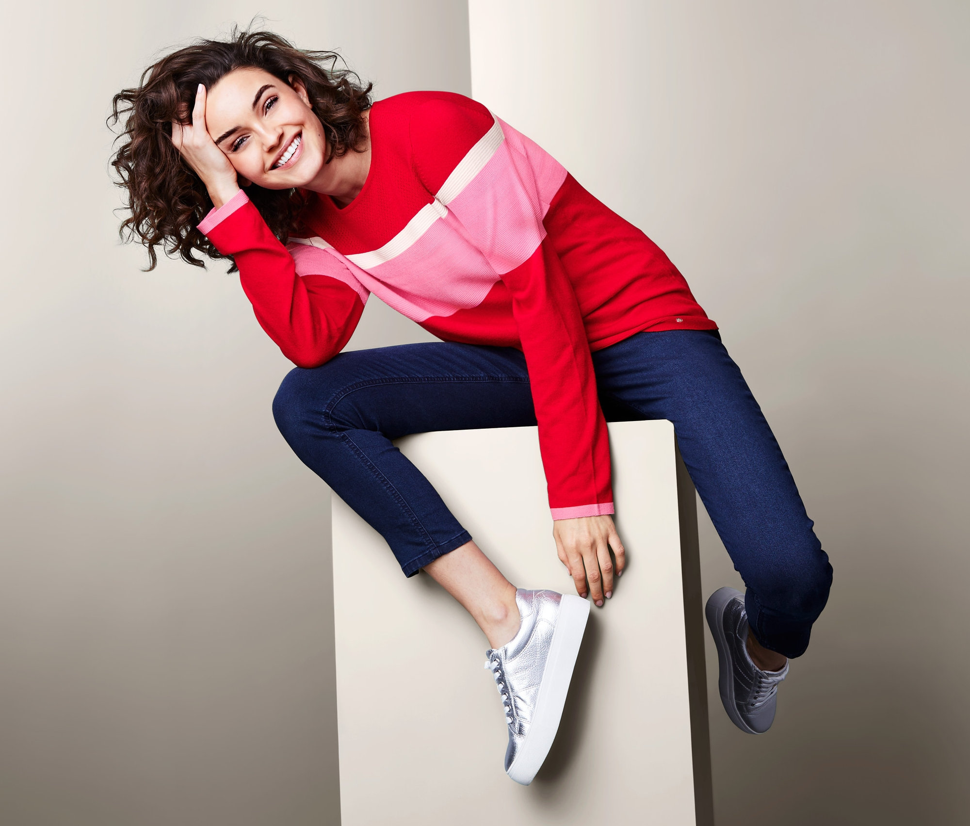 Kobieta siedzi na kostce i ma na sobie damski sweter w stylu color-blocking, czerwono-różowo-biały.