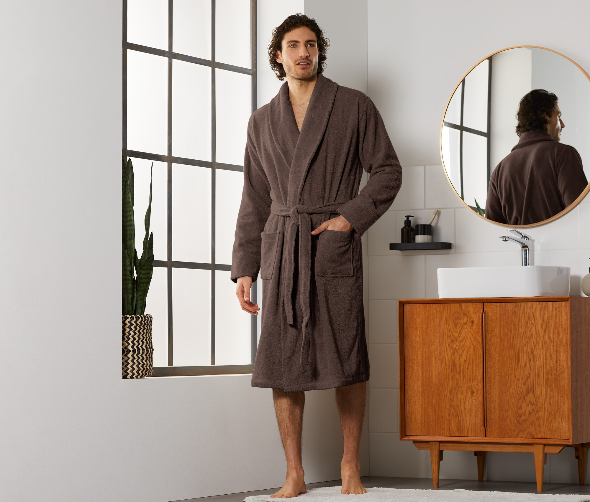 Mężczyzna stoi w łazience ubrany w brązowy męski szlafrok.