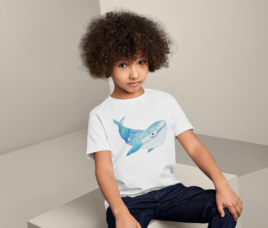 Chłopiec siedzi i ma na sobie bawełnianą koszulkę z nadrukiem wieloryba.