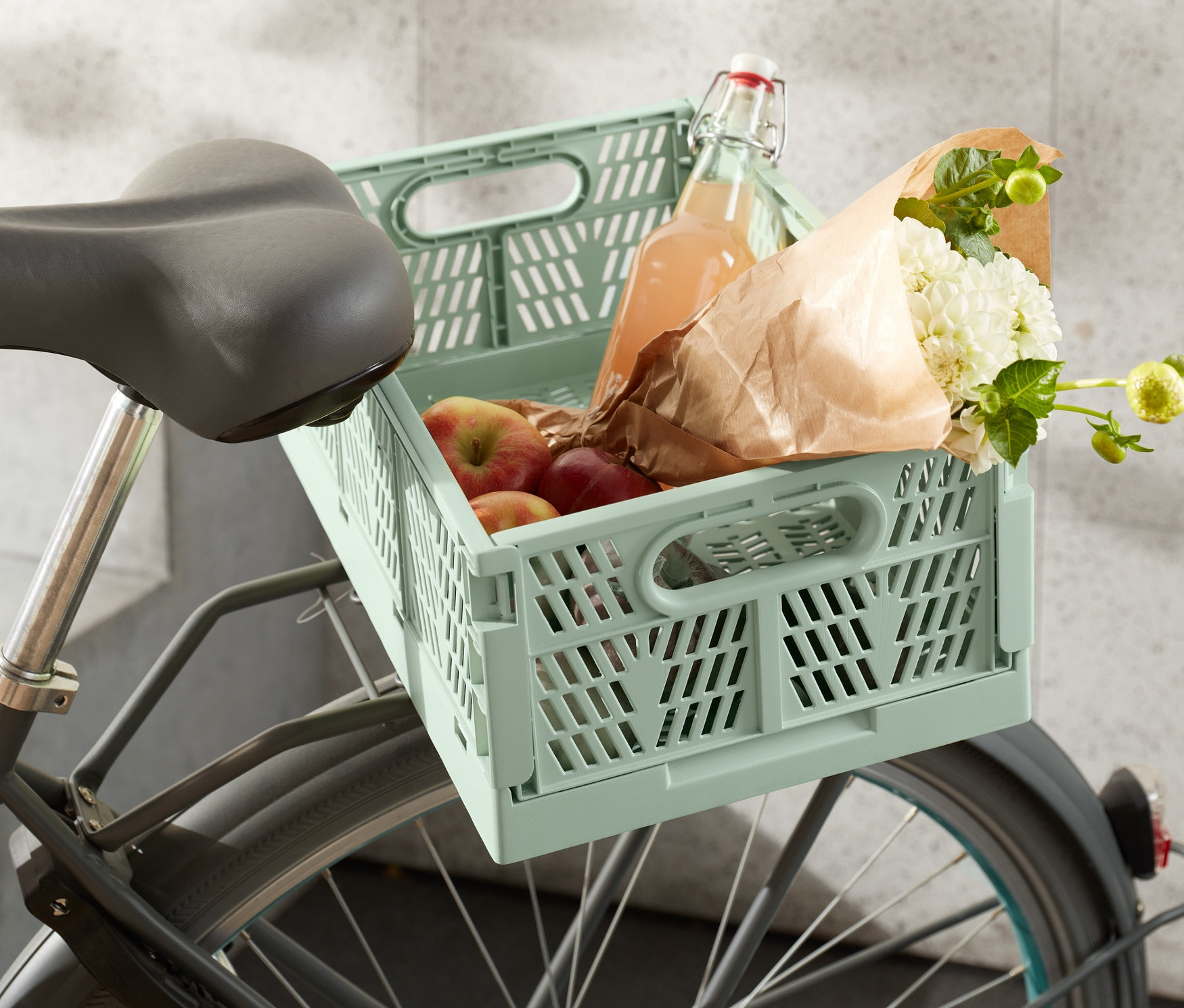 Na rowerze umieszczona jest składana skrzynka na rower miejski z jabłkami, kwiatami i butelką.