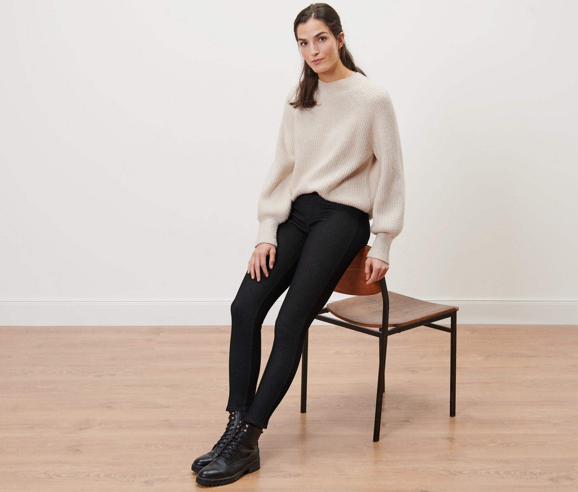 Kobieta siedzi na krześle i ma na sobie ocieplane legginsy stylizowane na dżinsy, sweter i buty.