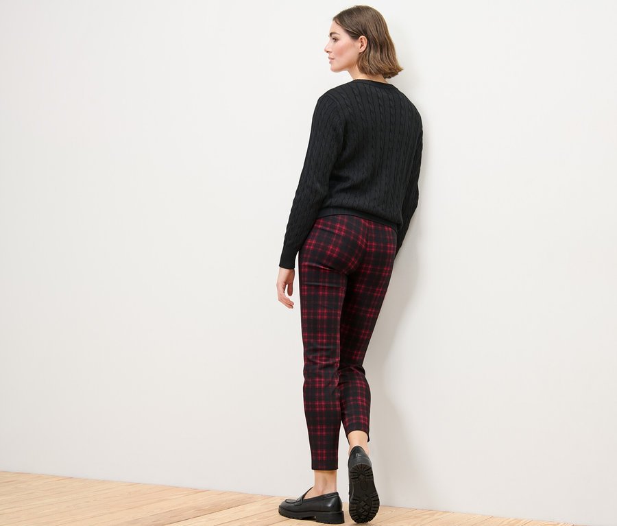 Kobieta stoi tyłem do kamery, ubrana w spodnie stretchowe w kratę, czarny sweter i czarne buty.