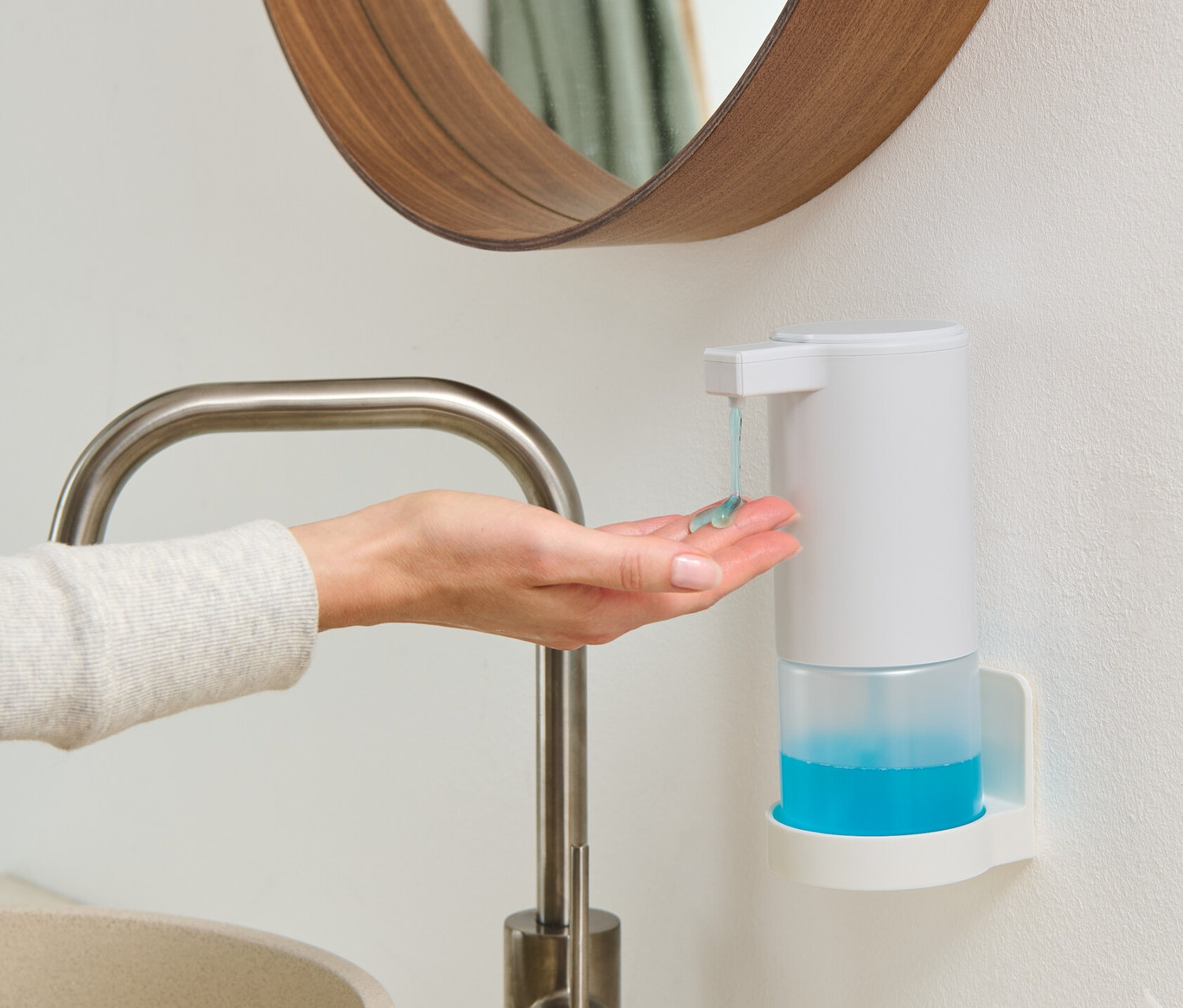 Kobieta aplikuje mydło z białego dozownika mydła z czujnikiem, zamontowanego na ścianie, na dłoń.