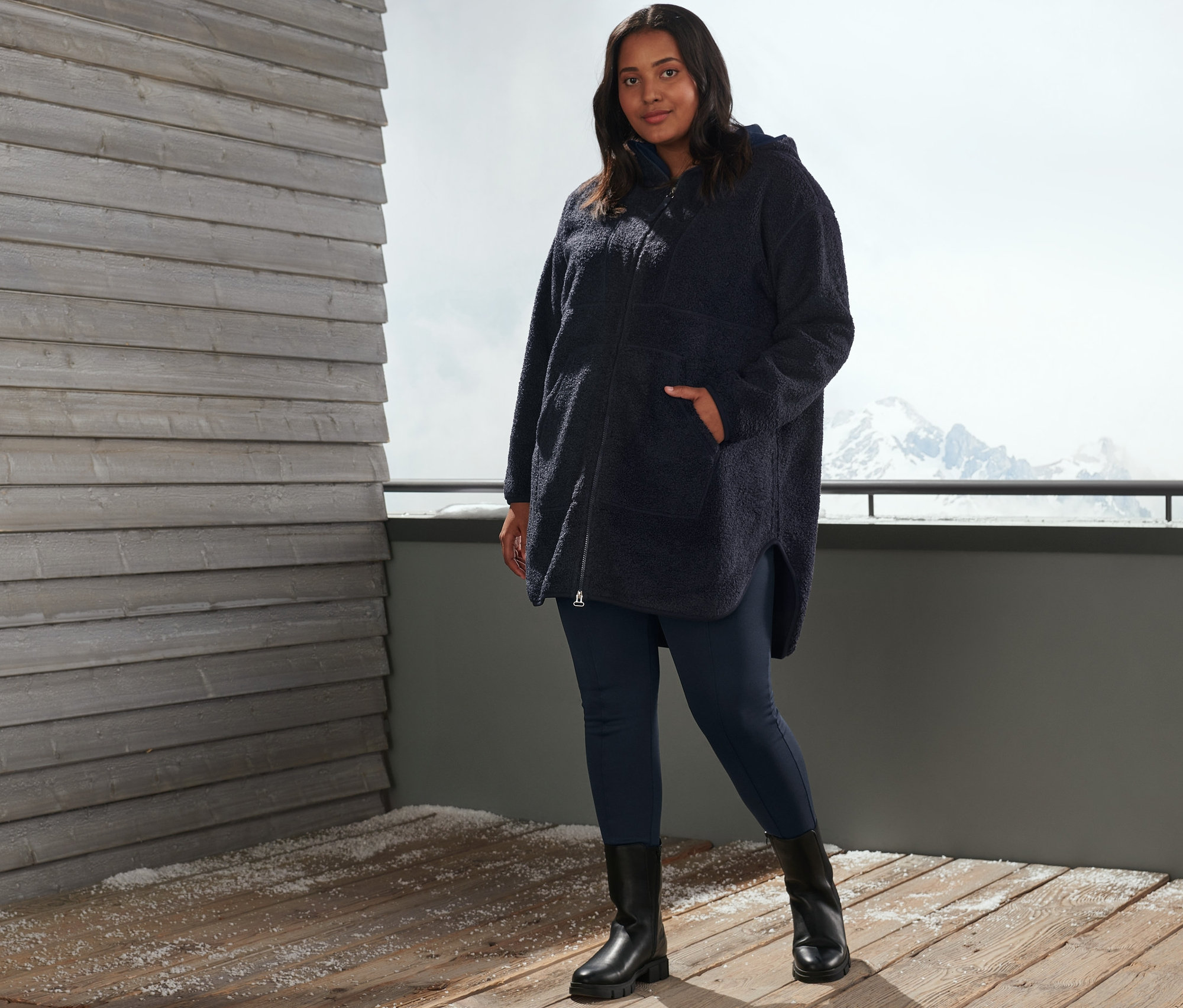 Kobieta pozuje na zewnątrz w niebieskich ocieplanych legginsach i płaszczu pluszowym oversize.