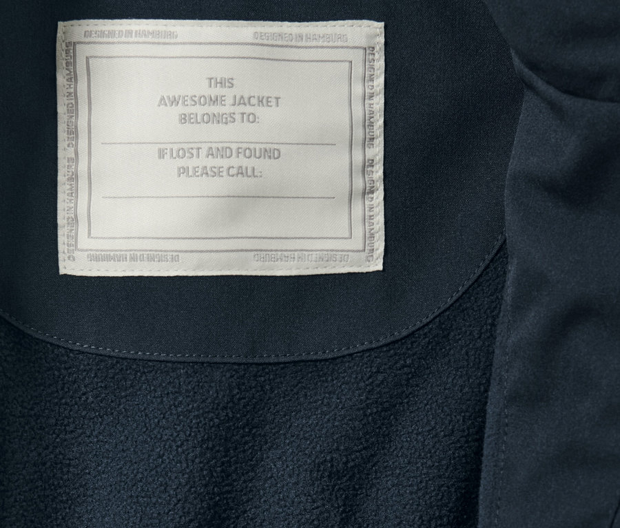 Zbliżenie na dziecięcą parkę przeciwdeszczową z etykietą 'THIS AWESOME JACKET BELONGS TO:'.