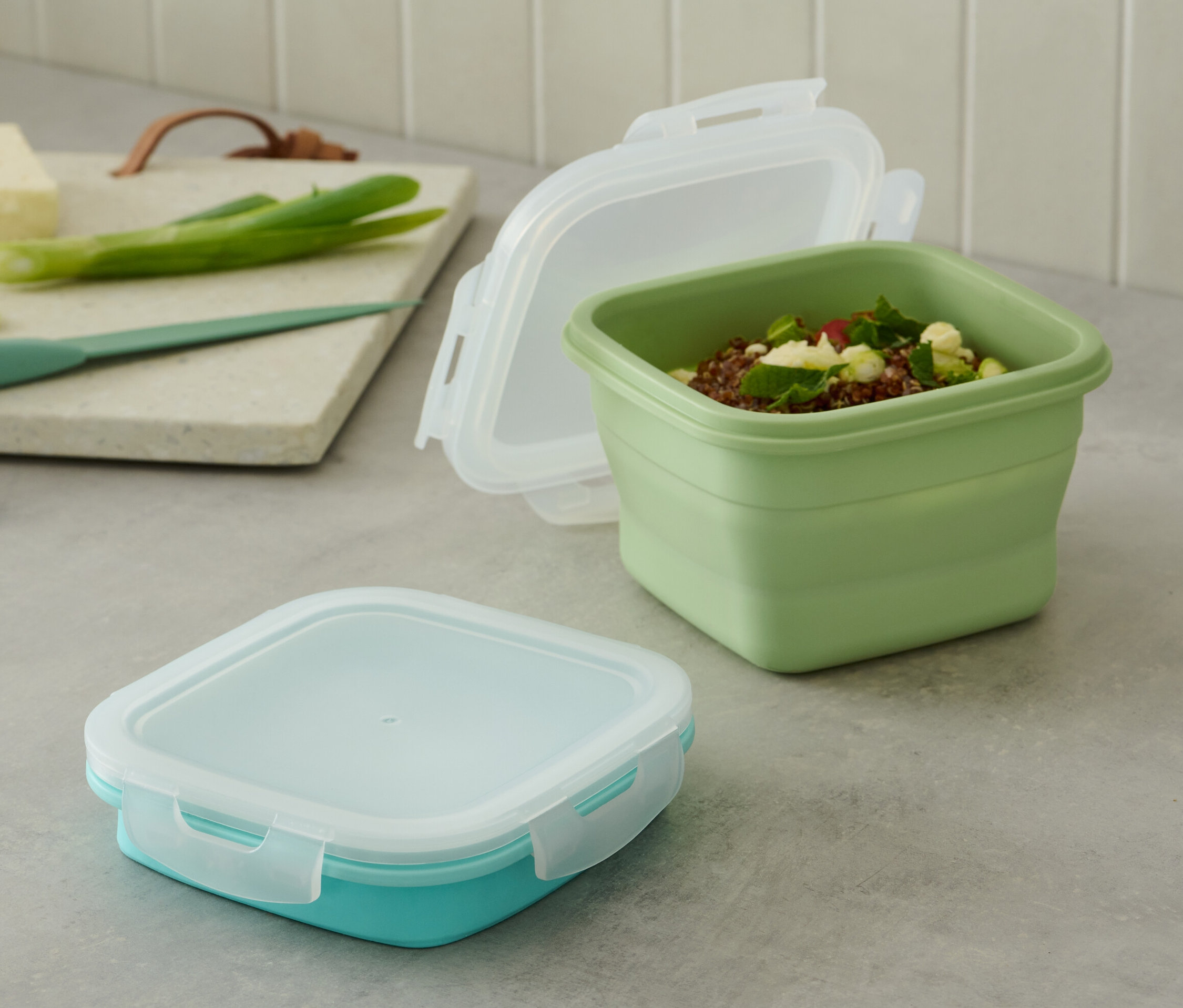 Na stole stoją 2 pojemniki spożywcze. Jeden pojemnik jest zielony i otwarty, drugi turkusowy i zamknięty.