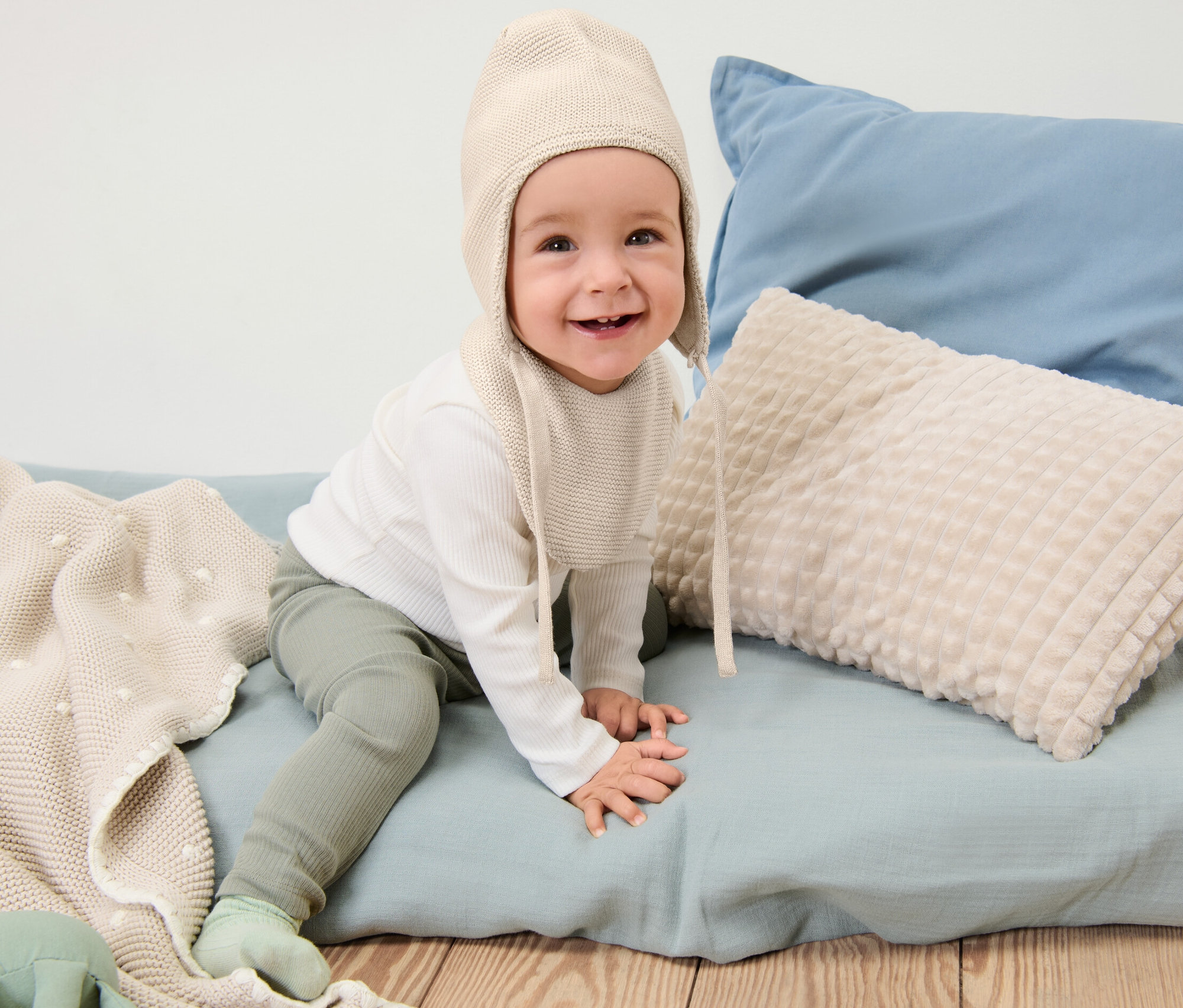 Uśmiechnięte dziecko siedzi i ma na sobie czapkę i szalik z dzianiny dla niemowląt.