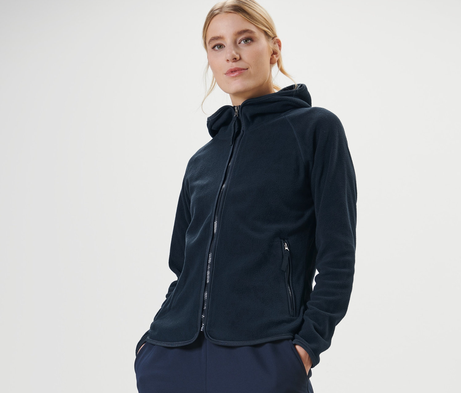 Kobieta pozuje w granatowej bluzie polarowej z kapturem.