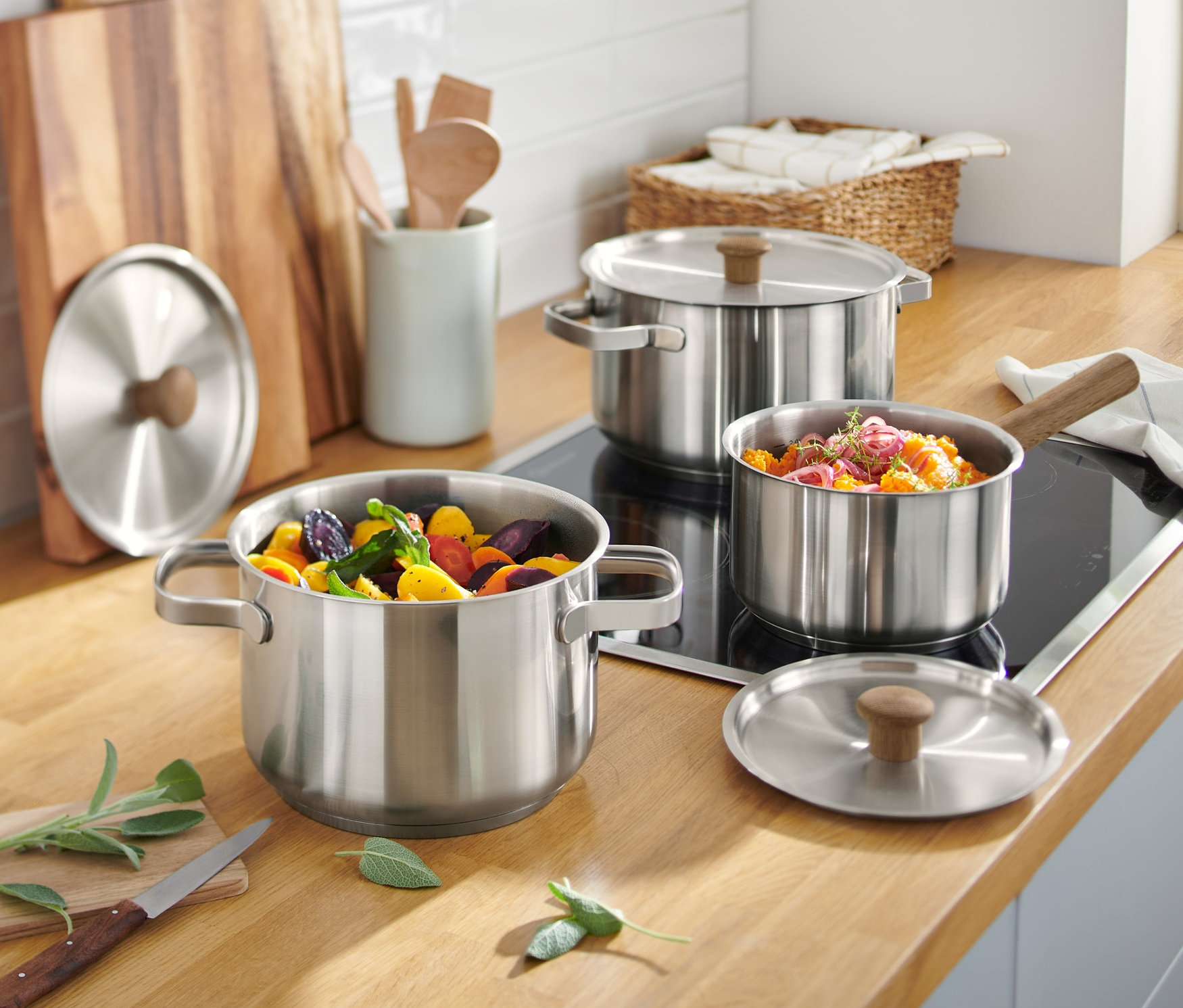 Zestaw garnków ze stali nierdzewnej stoi na drewnianym blacie kuchennym.