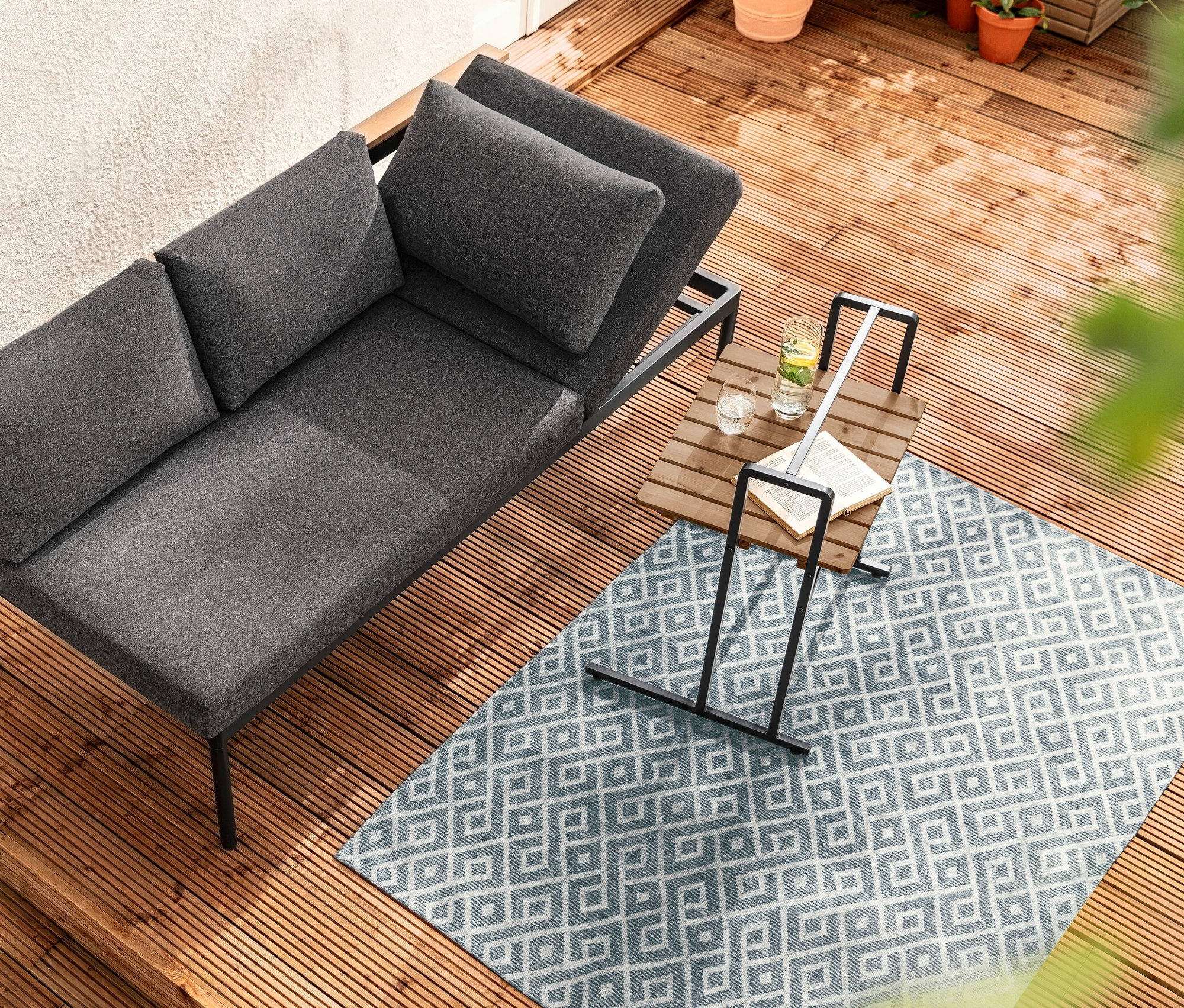 Widok z góry na ławę do jadalni i leżankę 2 w 1 „Elin” obok stolika w kształcie litery C z dużym blatem na drewnianym tarasie.