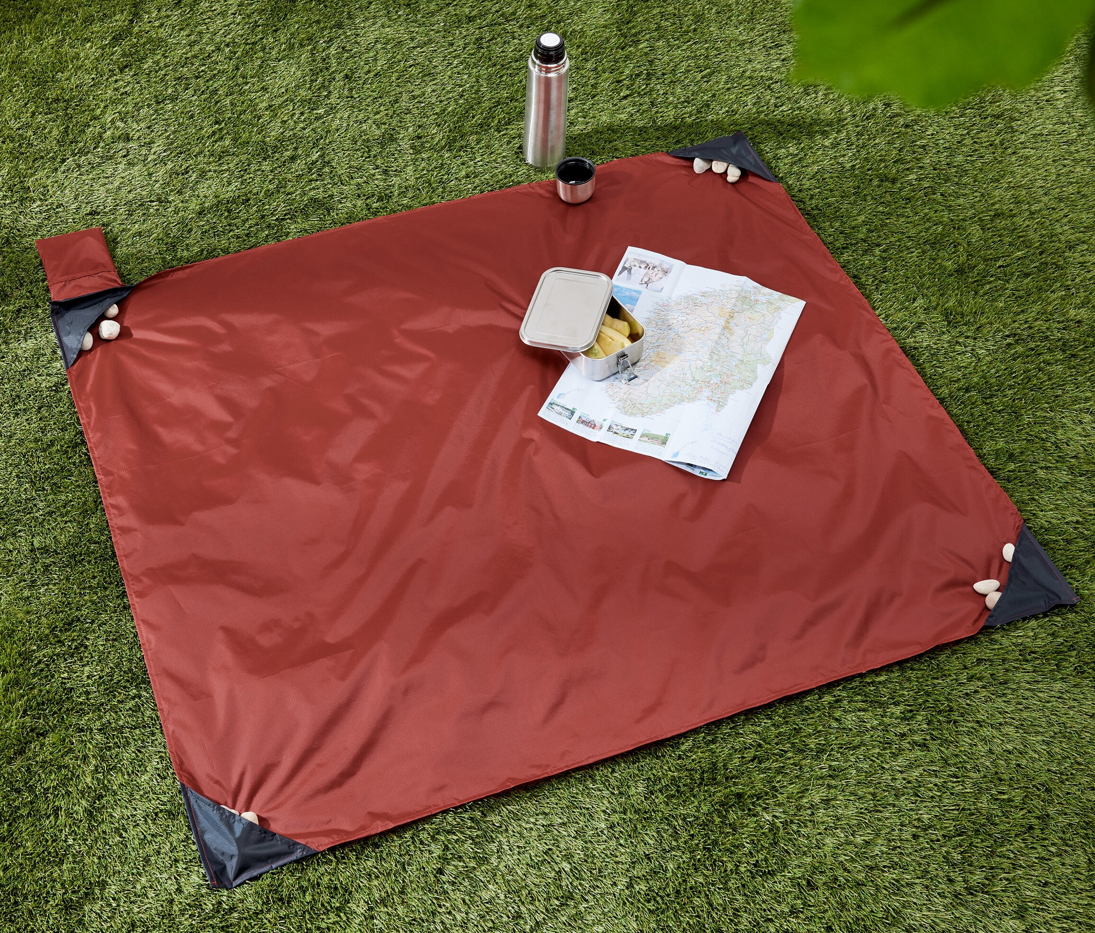 Na trawie leży minikoc piknikowy, na którym znajduje się mapa i przekąska. Obok koca stoi termos z kubkiem.