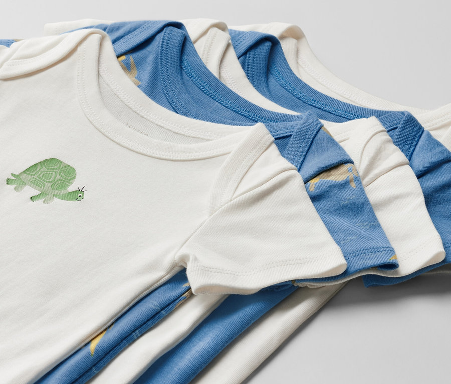 Zbliżenie na pięć body z krótkim rękawem dla niemowląt. Jedno białe body jest zadrukowane żółwiem.