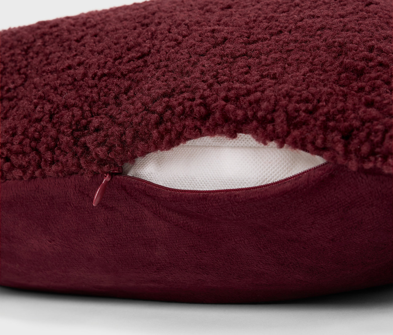 Szczegół bordowej, włochatej poduszki z zamkiem błyskawicznym.