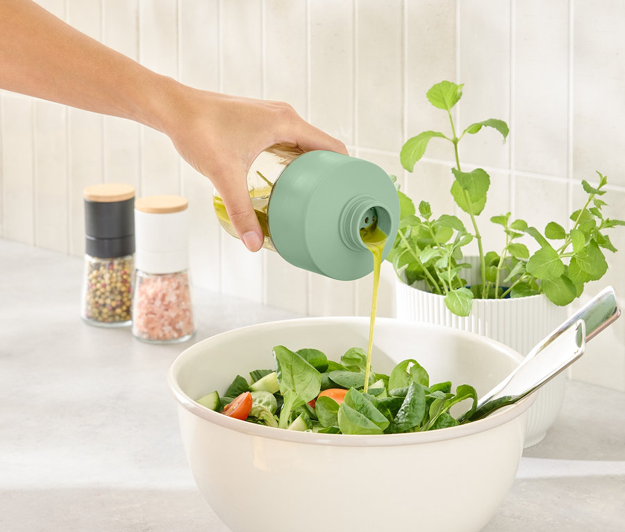 Ręka nalewa dressing z butelki na dressing do miski z sałatą.