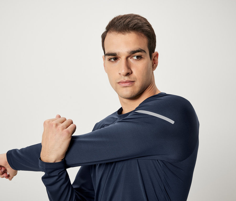 Mężczyzna rozciąga ramię w granatowej koszulce sportowej z długim rękawem.