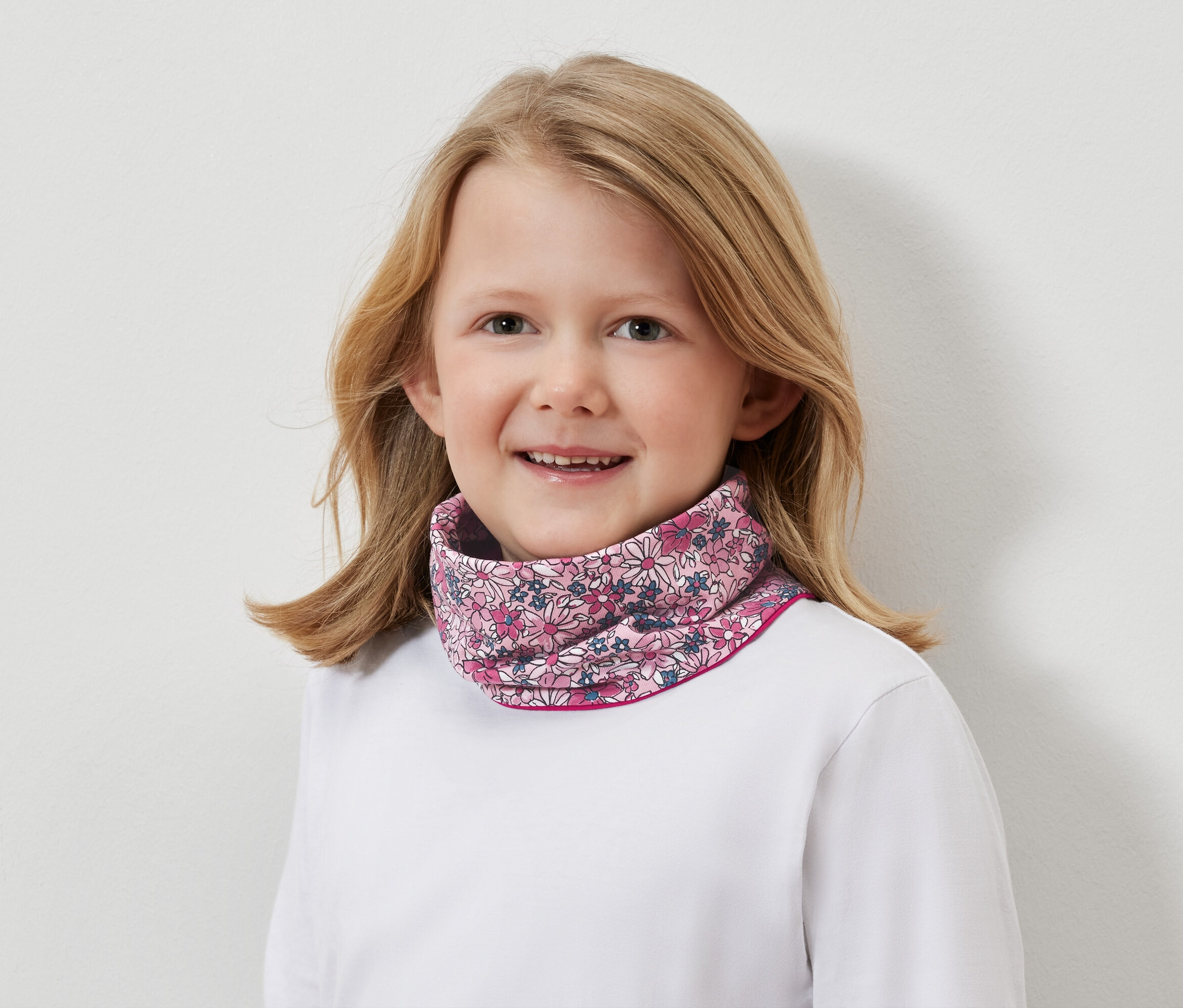 Portret uśmiechniętej blond dziewczynki w kwiecistym kominie.