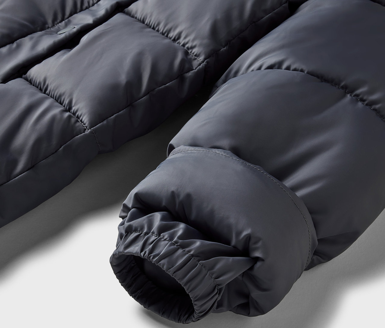 Zbliżenie na szarą kurtkę puchową z elastycznym mankietem.