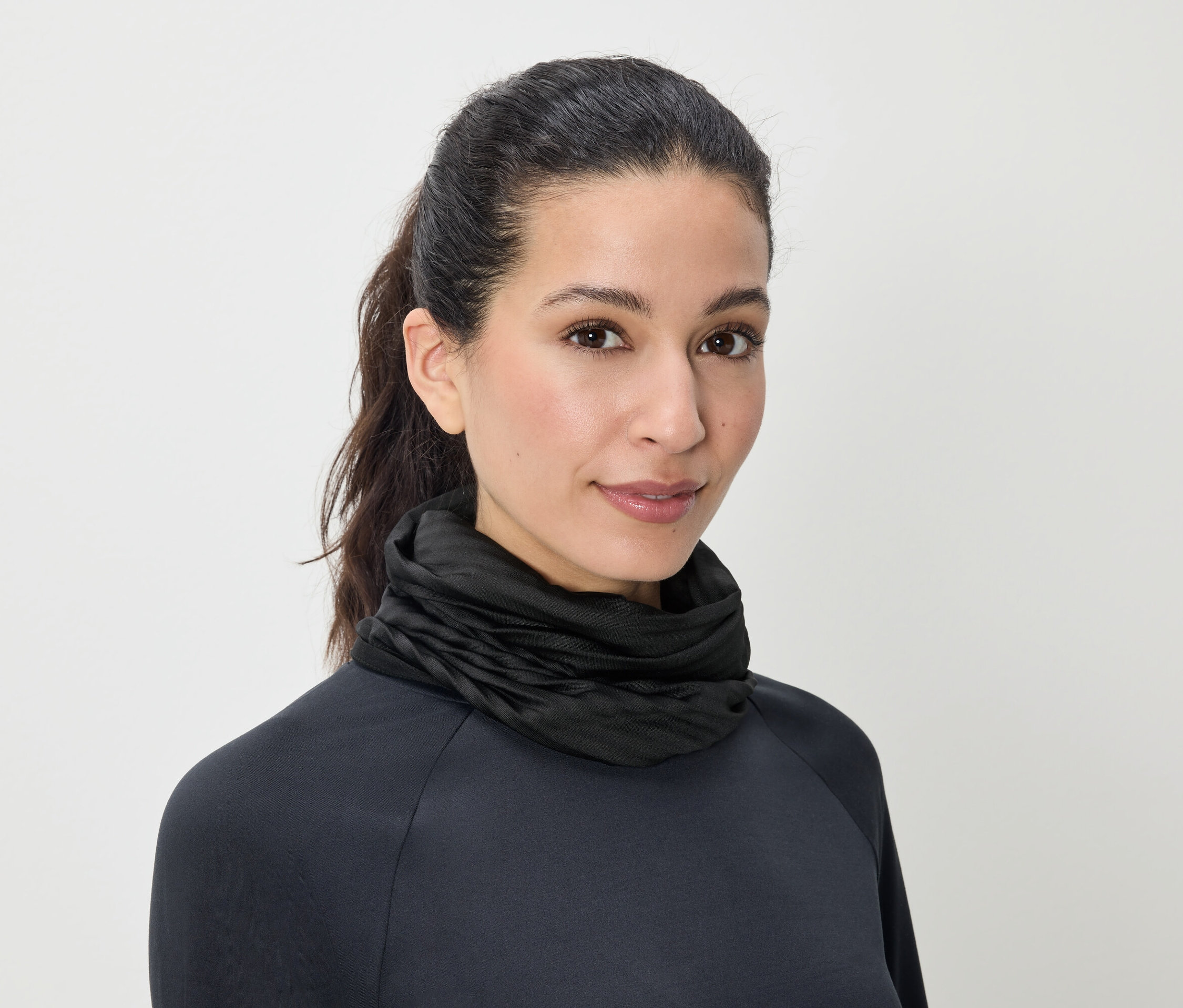 Portret kobiety z brązowymi włosami związanymi w kucyk, ubranej w czarny golf.