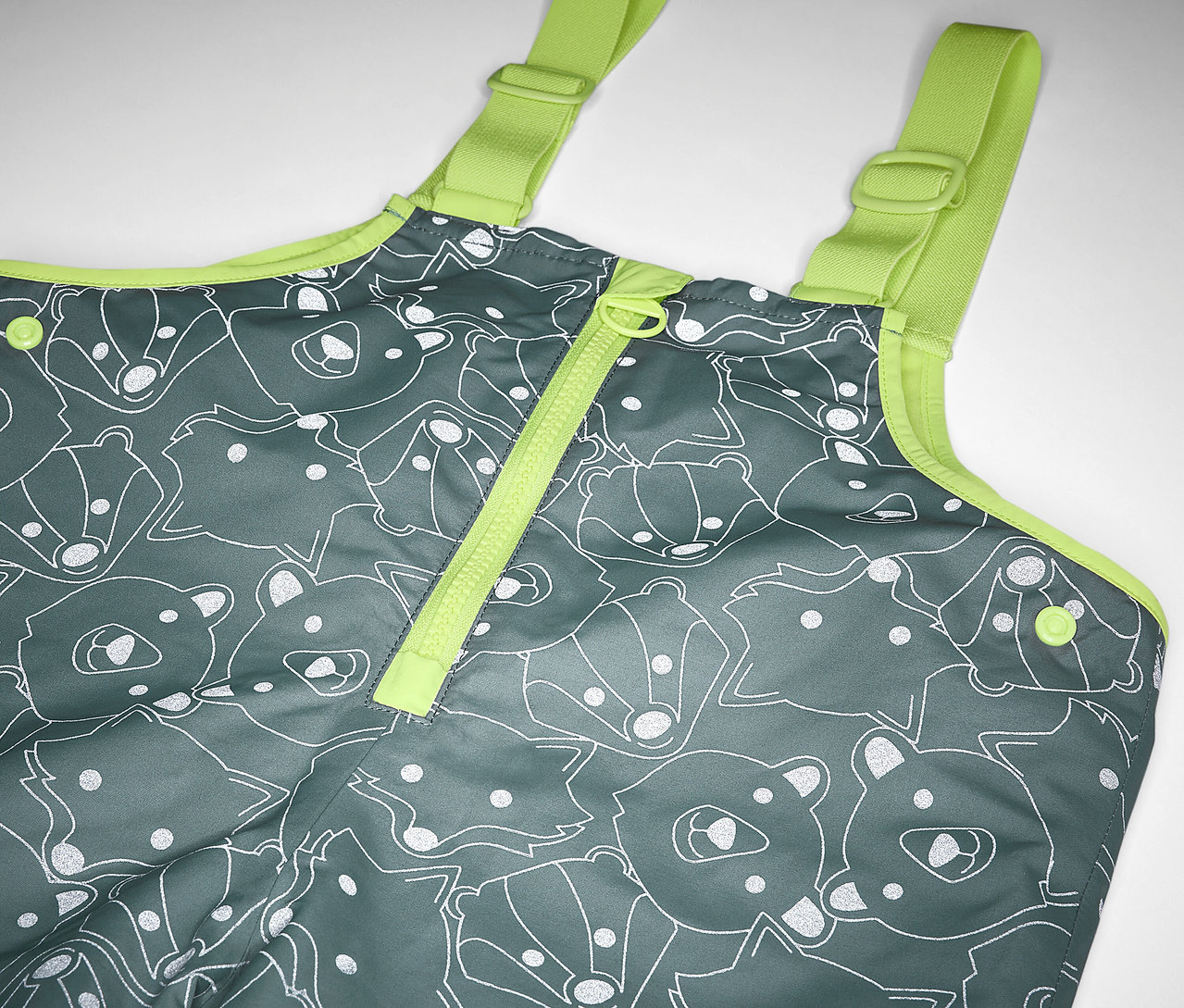 Zbliżenie na termoaktywne spodnie przeciwdeszczowe z elementami odblaskowymi dla dzieci, szare w misie i lisy, z żółtymi ramiączkami.