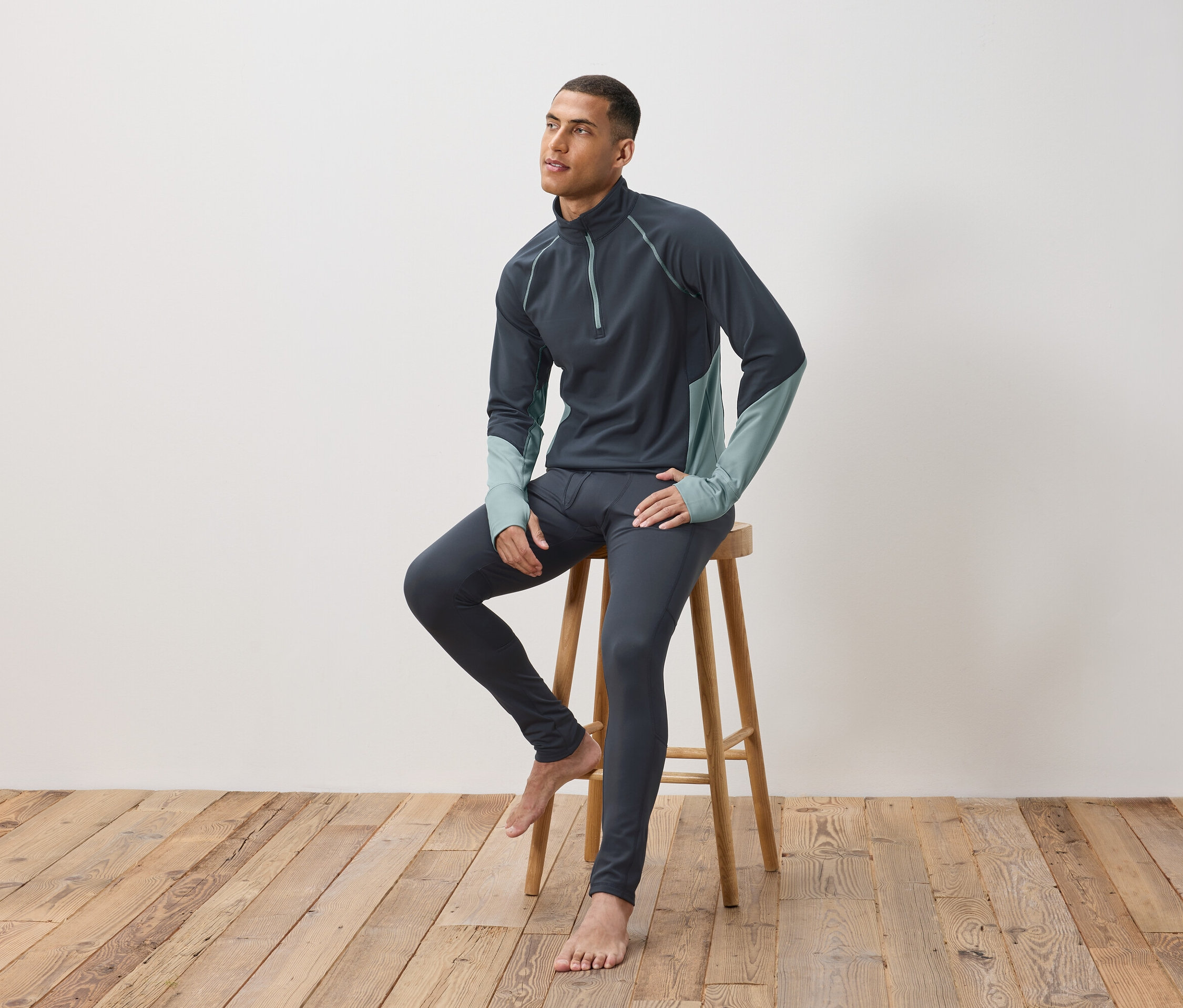 Mężczyzna siedzi na drewnianym stołku, ubrany w ciemnoszarą bieliznę termoaktywną.