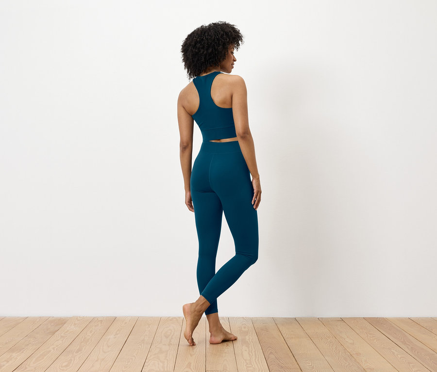 Z tyłu widać kobietę o ciemnych włosach, ubraną w niebieski biustonosz sportowy i legginsy.