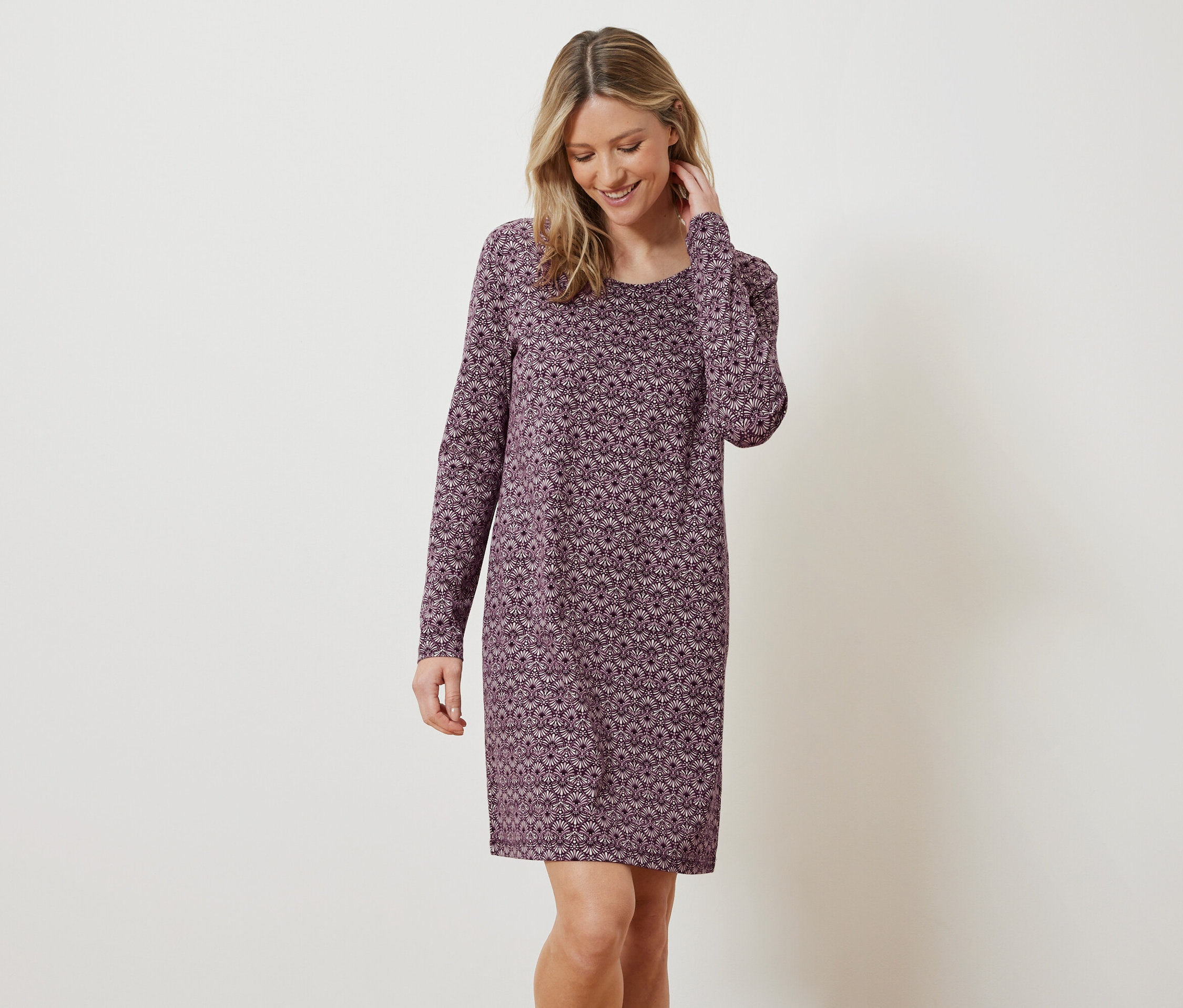 Uśmiechnięta blondynka pozuje w kwiecistej sukience z długim rękawem.