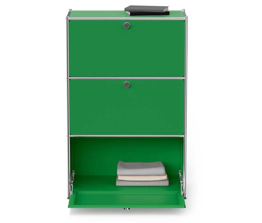 Zielona szafka z trzema półkami, dwie górne zamknięte, na górnej półce leży książka, dolna półka jest otwarta i znajdują się w niej złożone ręczniki.