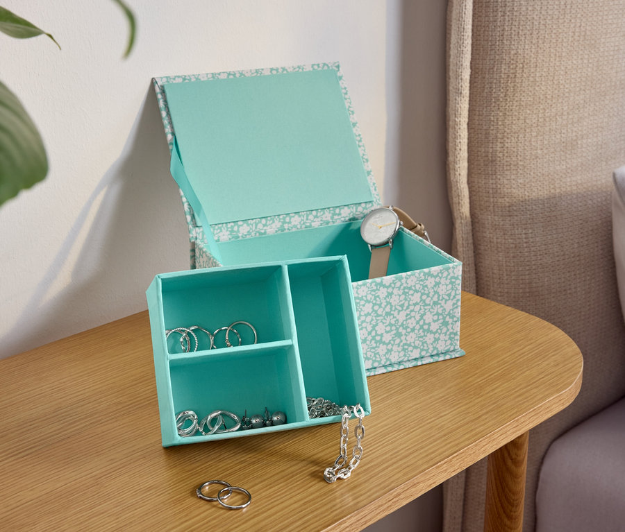 Turkusowe pudełko na biżuterię we wzory kwiatowe na drewnianym stoliku nocnym.