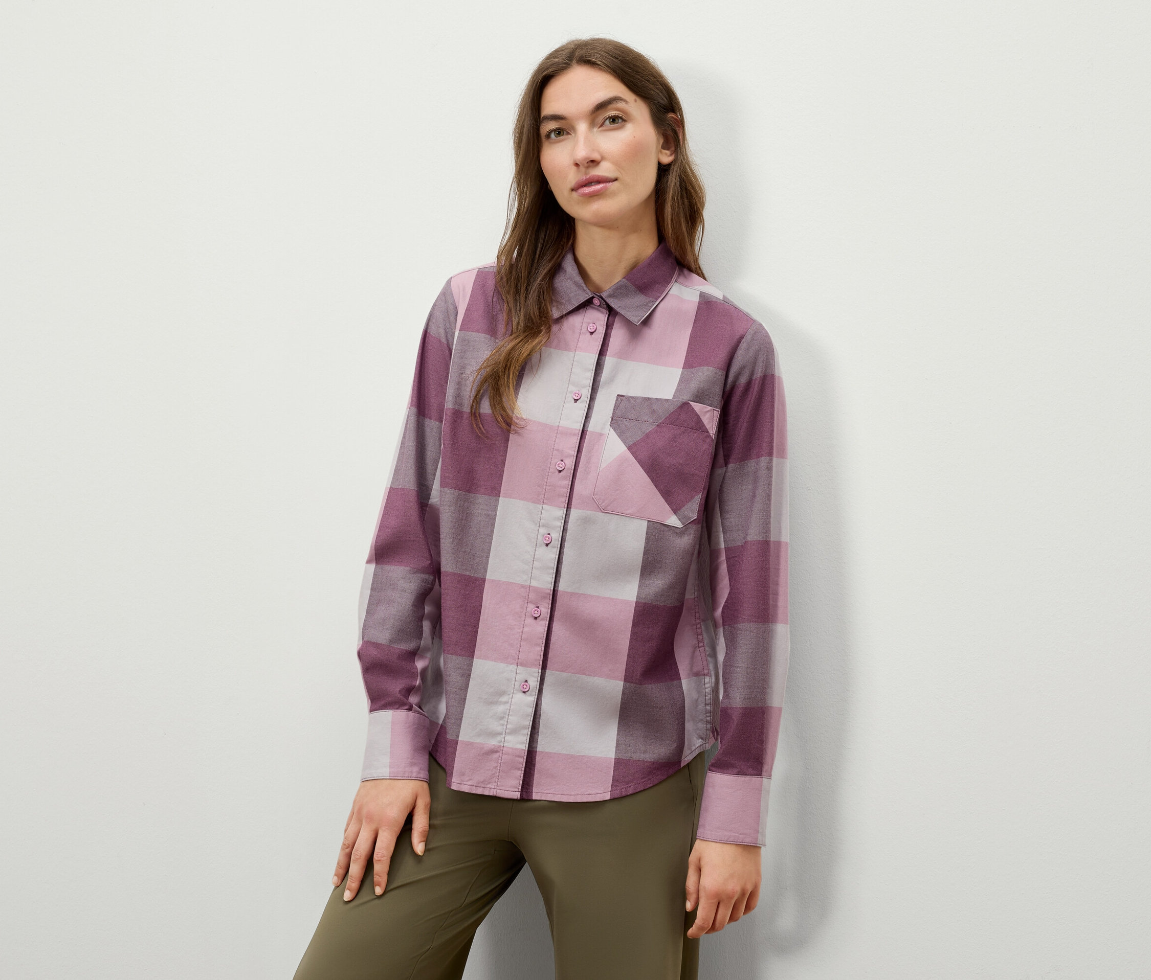 Kobieta pozuje w kraciastej koszuli z długim rękawem i oliwkowozielonych spodniach.