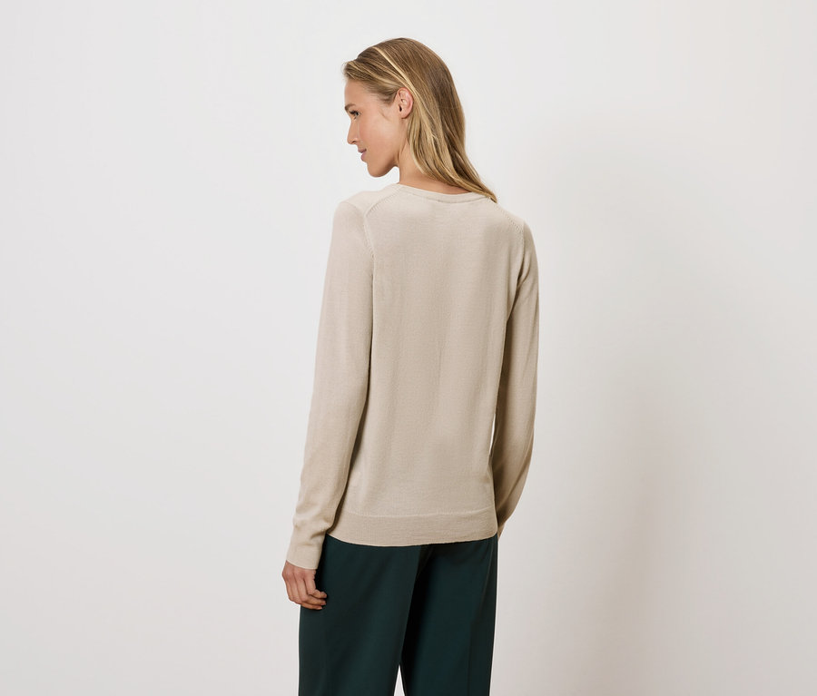 Kobieta spogląda przez ramię, ubrana w beżowy sweter i zielone spodnie.