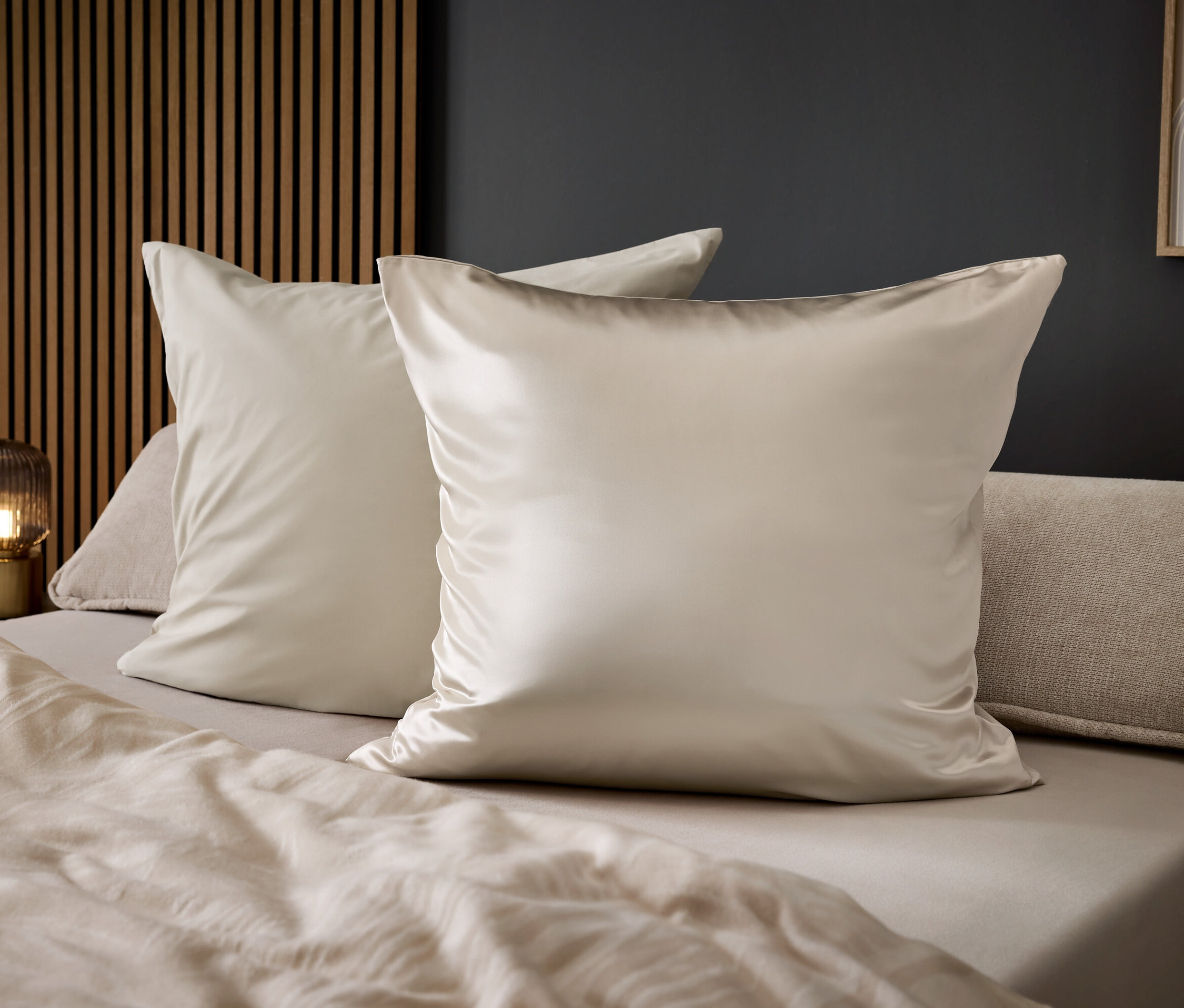 Dwie błyszczące, beżowe poduszki na łóżku z beżowymi prześcieradłami.