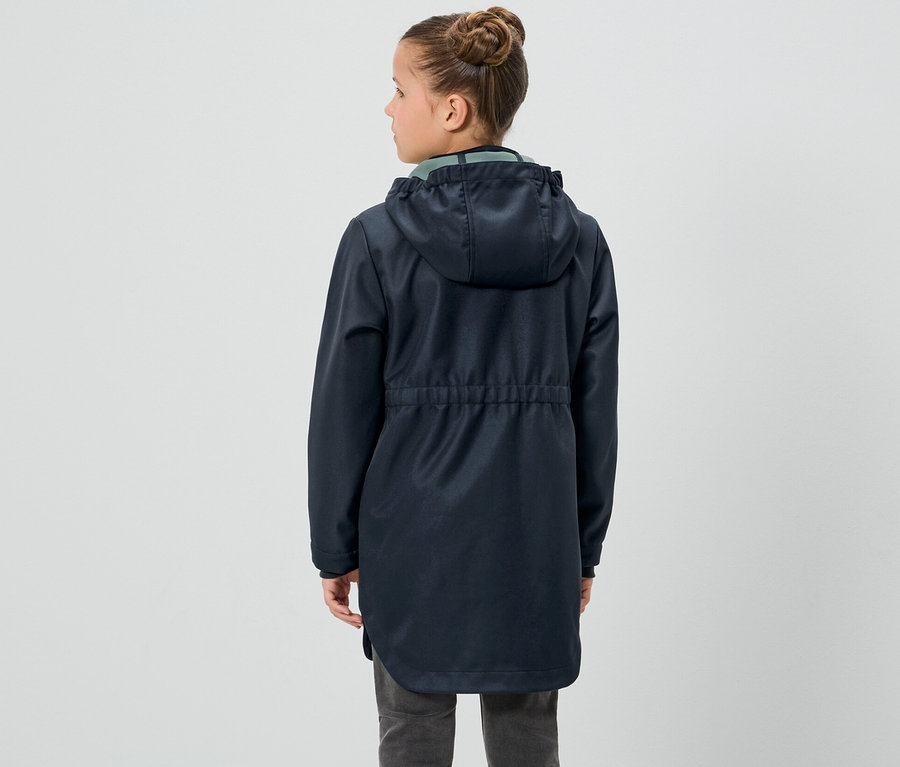 Dziewczyna stoi tyłem, ubrana w kurtkę softshell dla dzieci.