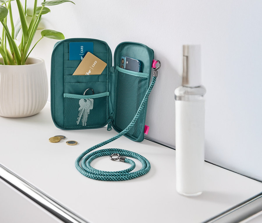 Otwarty, zielony portfel leży na białym stole, wypełniony kartami, kluczami i telefonem komórkowym.