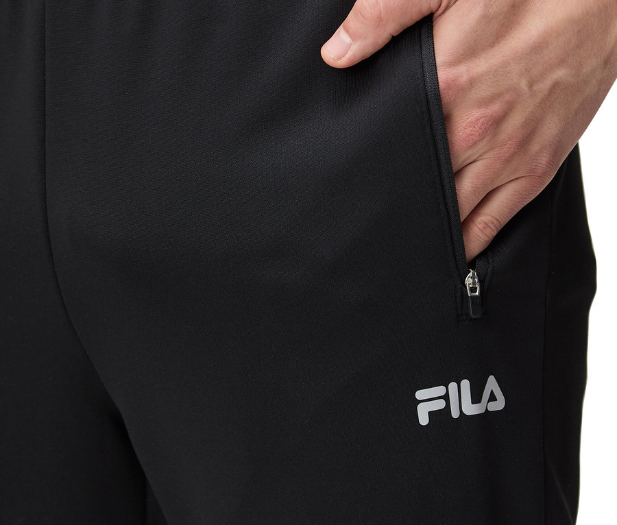 Mężczyzna wkłada rękę do kieszeni czarnych spodni dresowych FILA.