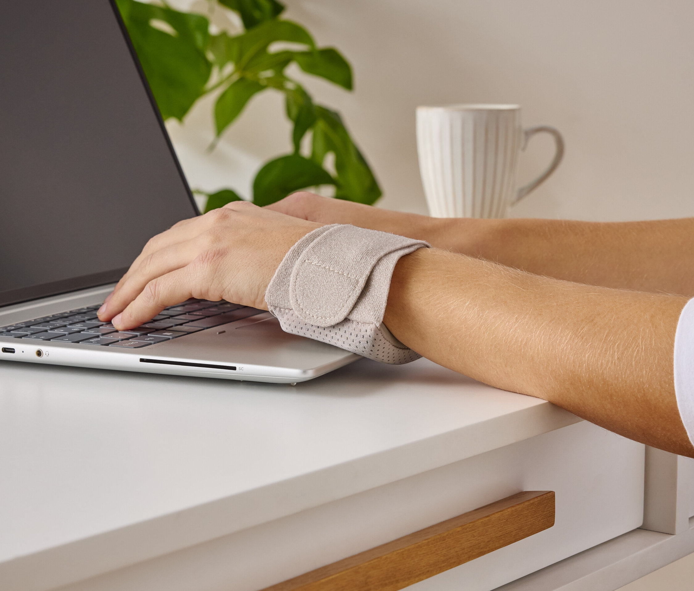 Osoba pisze na laptopie i nosi podparcie nadgarstka.