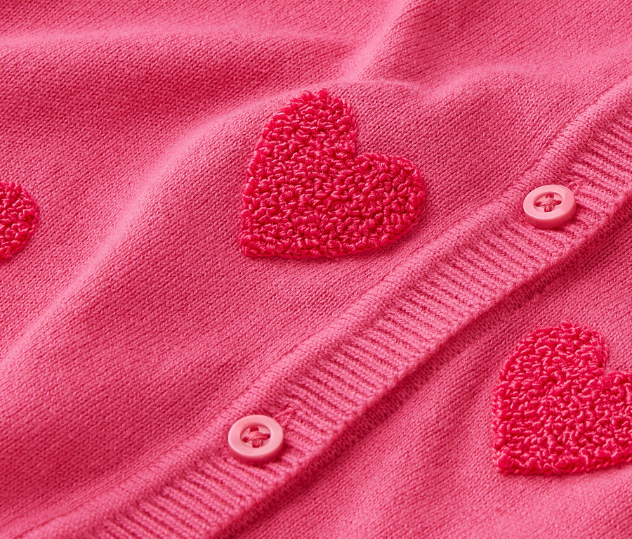 Zbliżenie na różowy kardigan z aplikacjami w kształcie serc i guzikami.