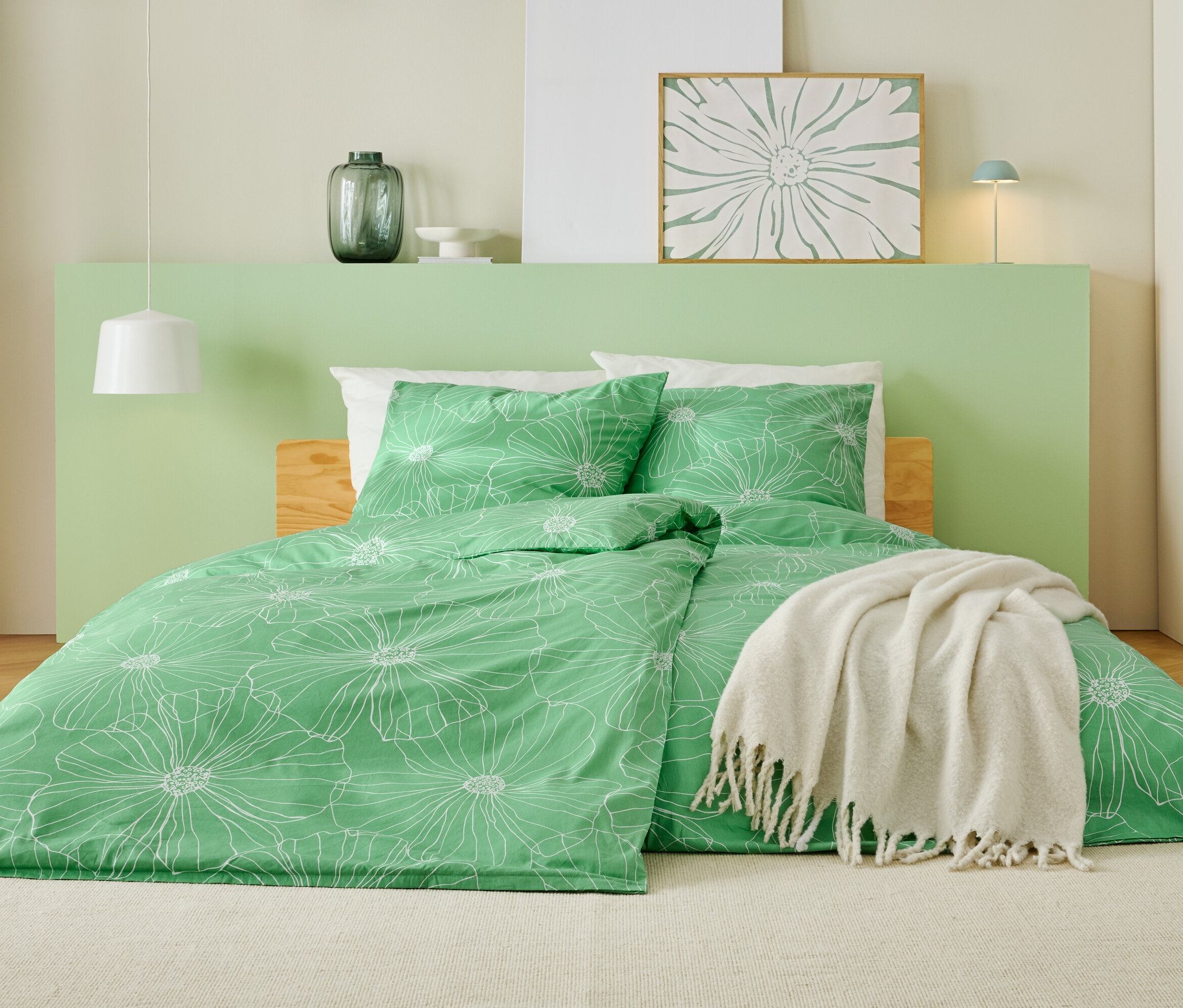 Łóżko z zieloną pościelą w białe kwiaty, białym kocem i jasnozielonym zagłówkiem.