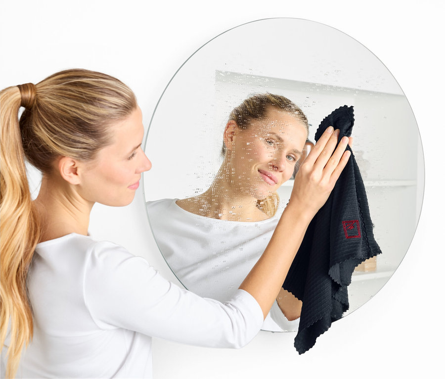 Kobieta czyści okrągłe lustro czarną ściereczką.