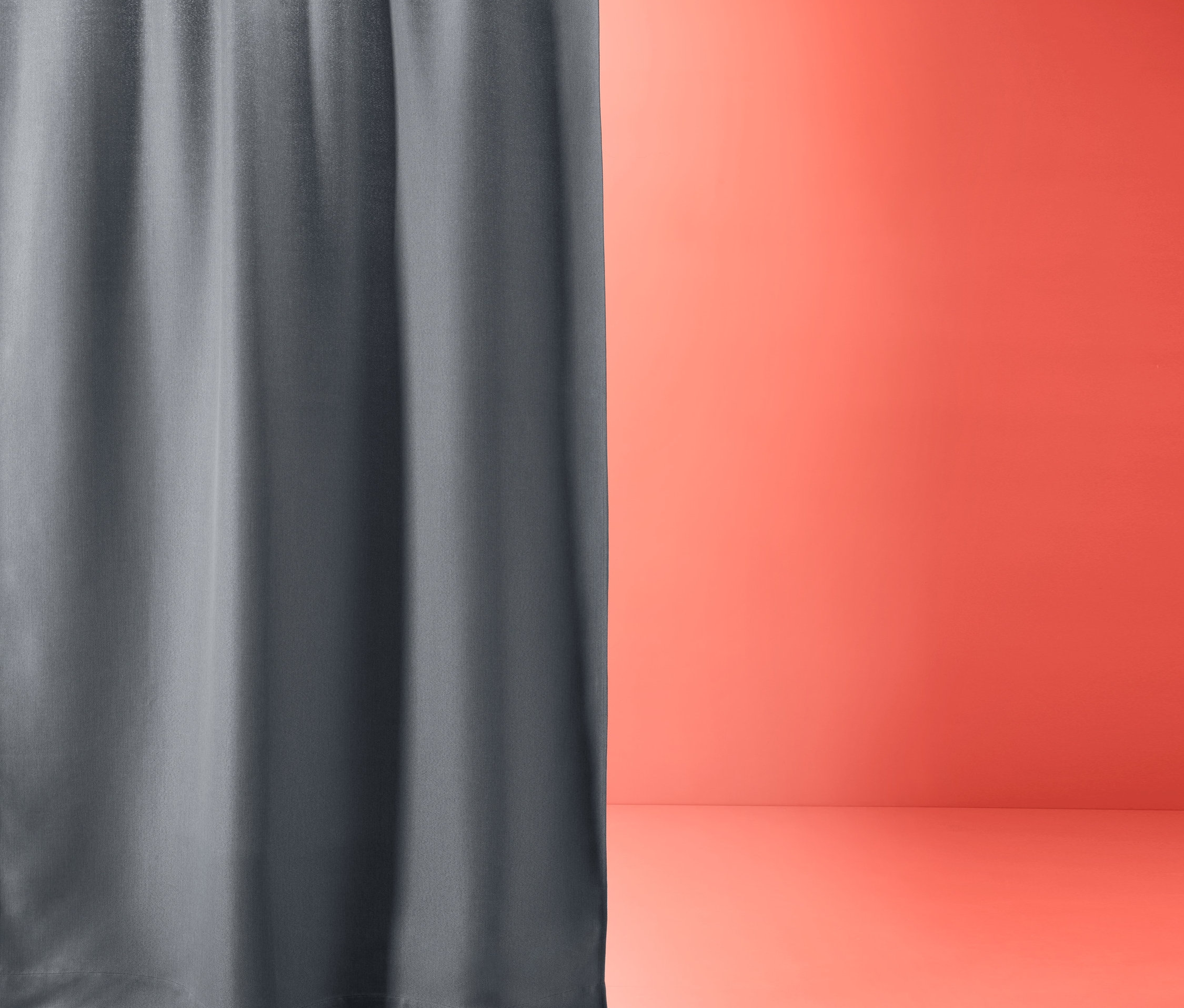 Szara zasłona zaciemniająca wisi na karniszu na tle pomarańczowej ściany. Zasłony zaciemniające szare, 2 sztuki.