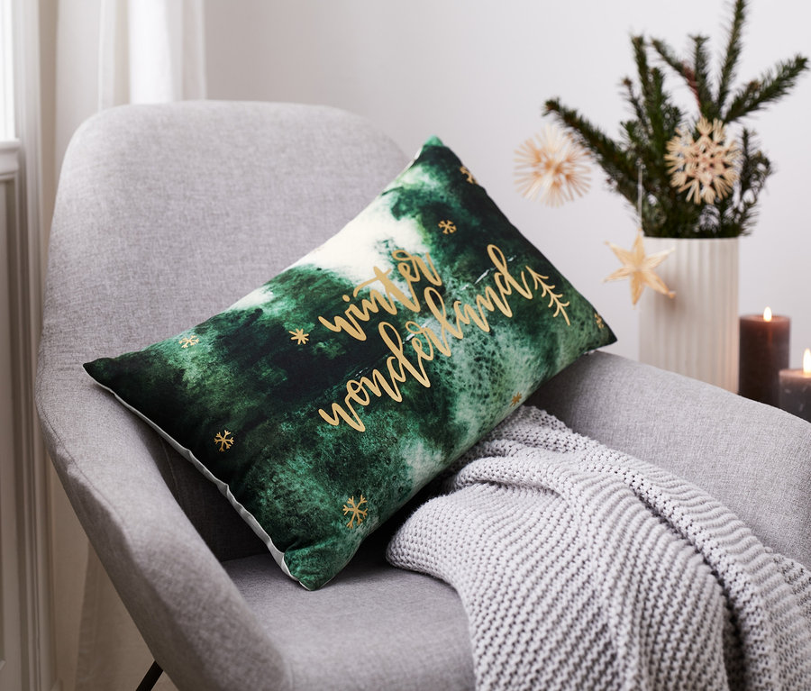 Poduszka dekoracyjna z motywem "Winter Wonderland" leży na szarym krześle.