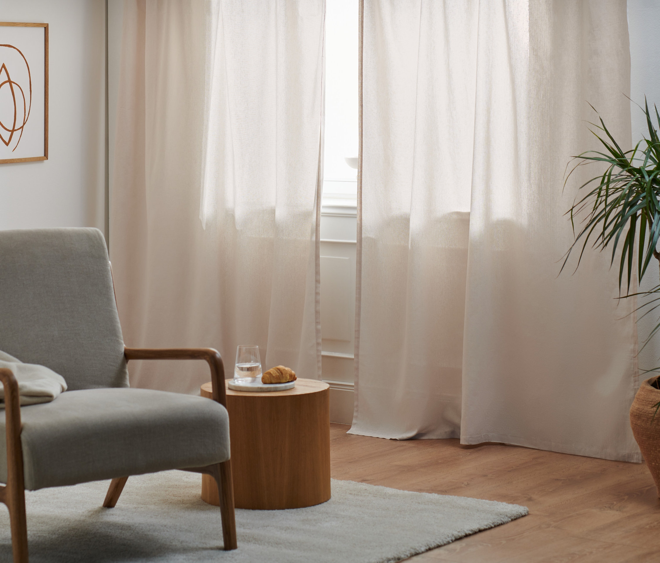 Szary fotel stoi obok okna z dwoma zasłonami z mieszanki lnu i bawełny.