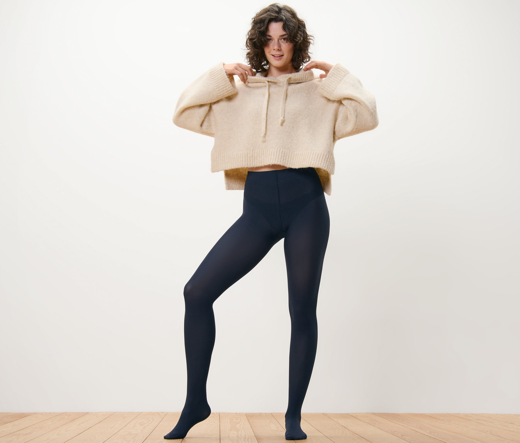 Kobieta pozuje w bezowej bluzie z kapturem i granatowych, cienkich rajstopach, 80 DEN, 2 pary.