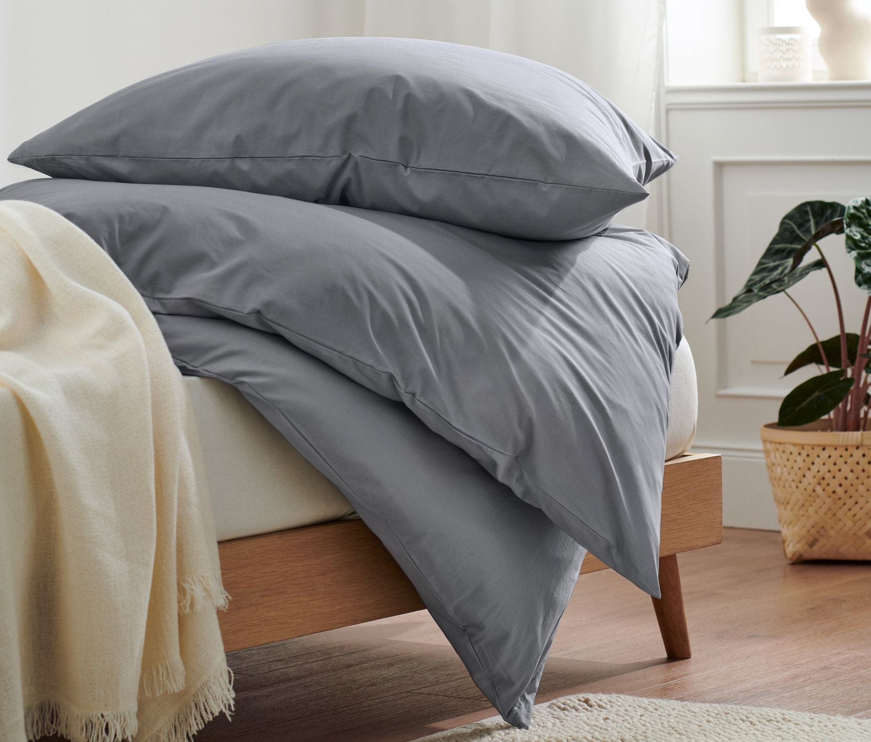 Stos szarej pościeli bawełnianej premium na łóżku z drewnianą ramą.