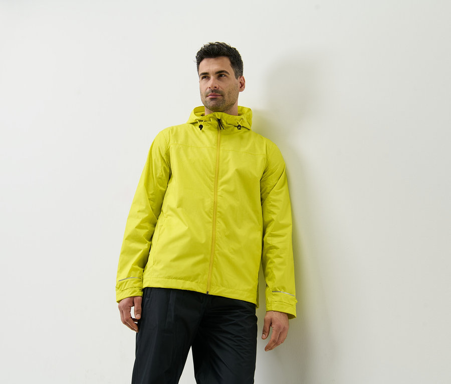 Mężczyzna opiera się o ścianę i ma na sobie żółtą kurtkę przeciwdeszczową.