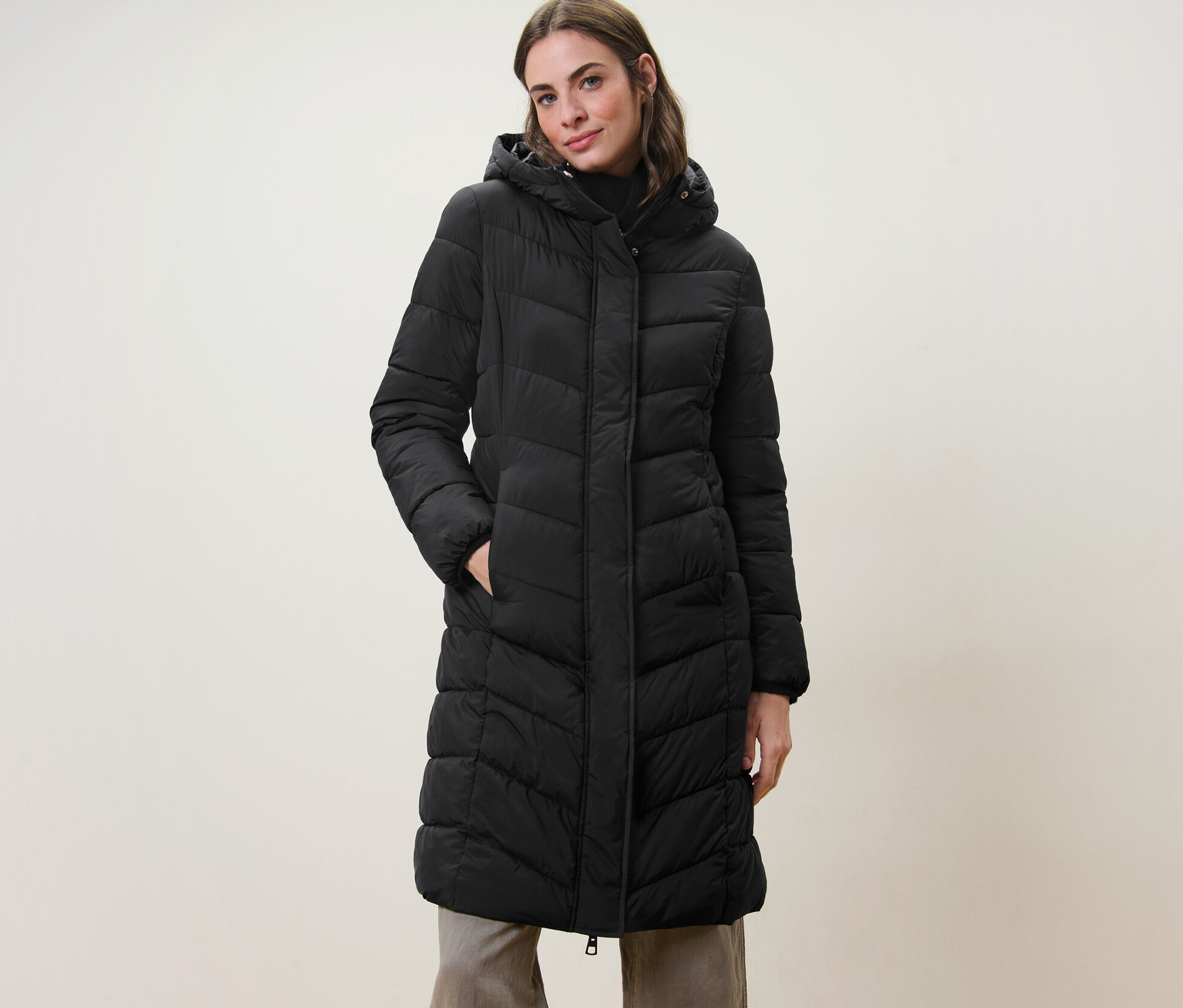 Kobieta pozuje w czarnym płaszczu pikowanym z kapturem.