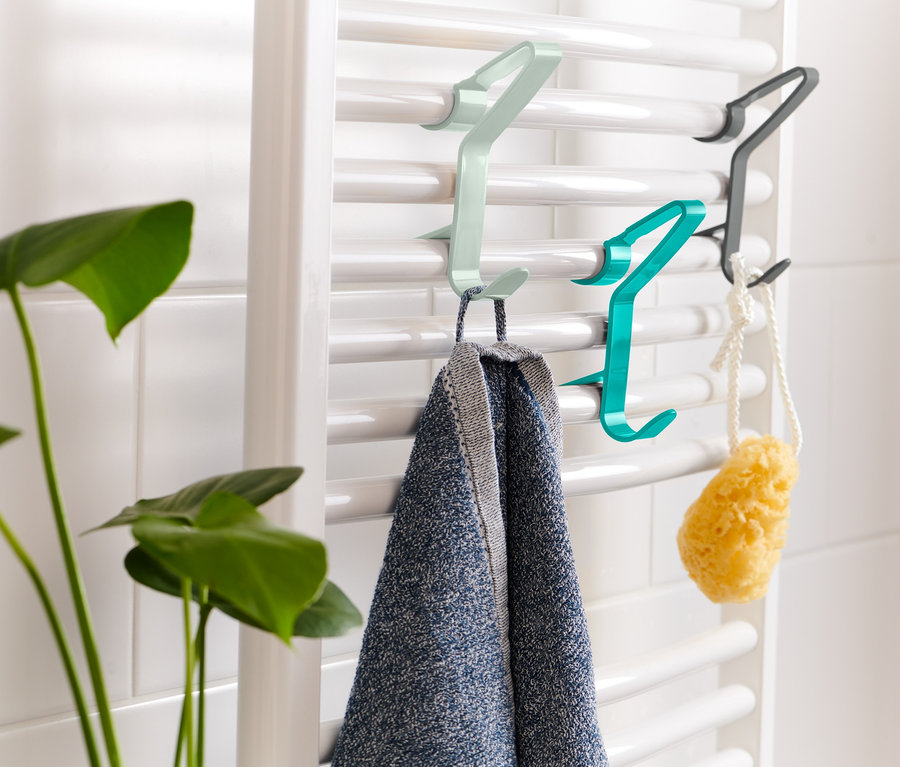 Na białym grzejniku wiszą 3 haczyki na grzejnik, na których wiszą ręcznik i gąbka.